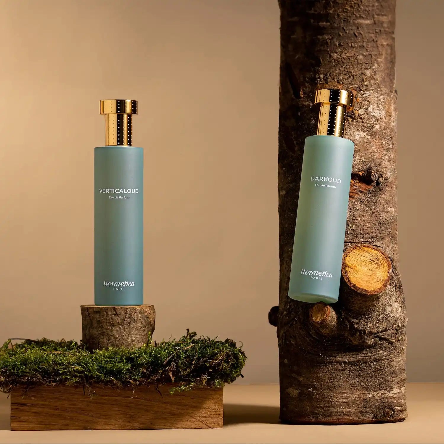 Two mint-green perfume bottles with gold caps displayed on wooden logs with moss.